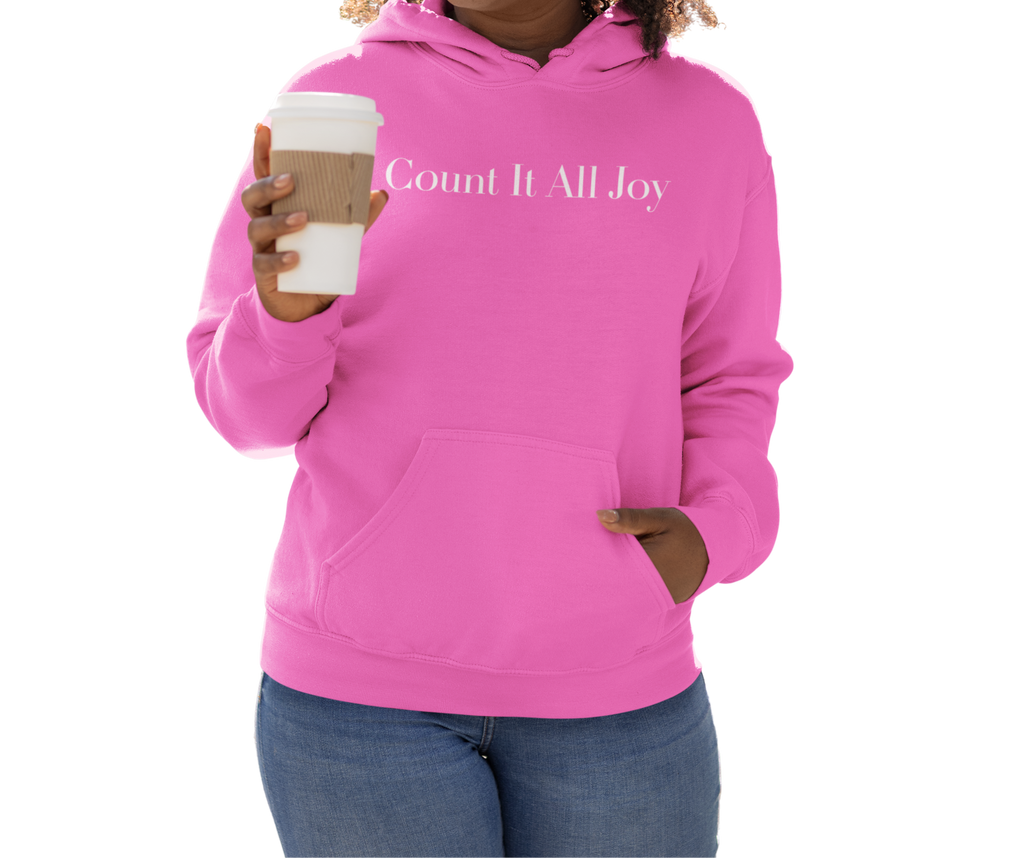 Person wearing a pink hoodie with 'Count It All Joy' text, holding a coffee cup.